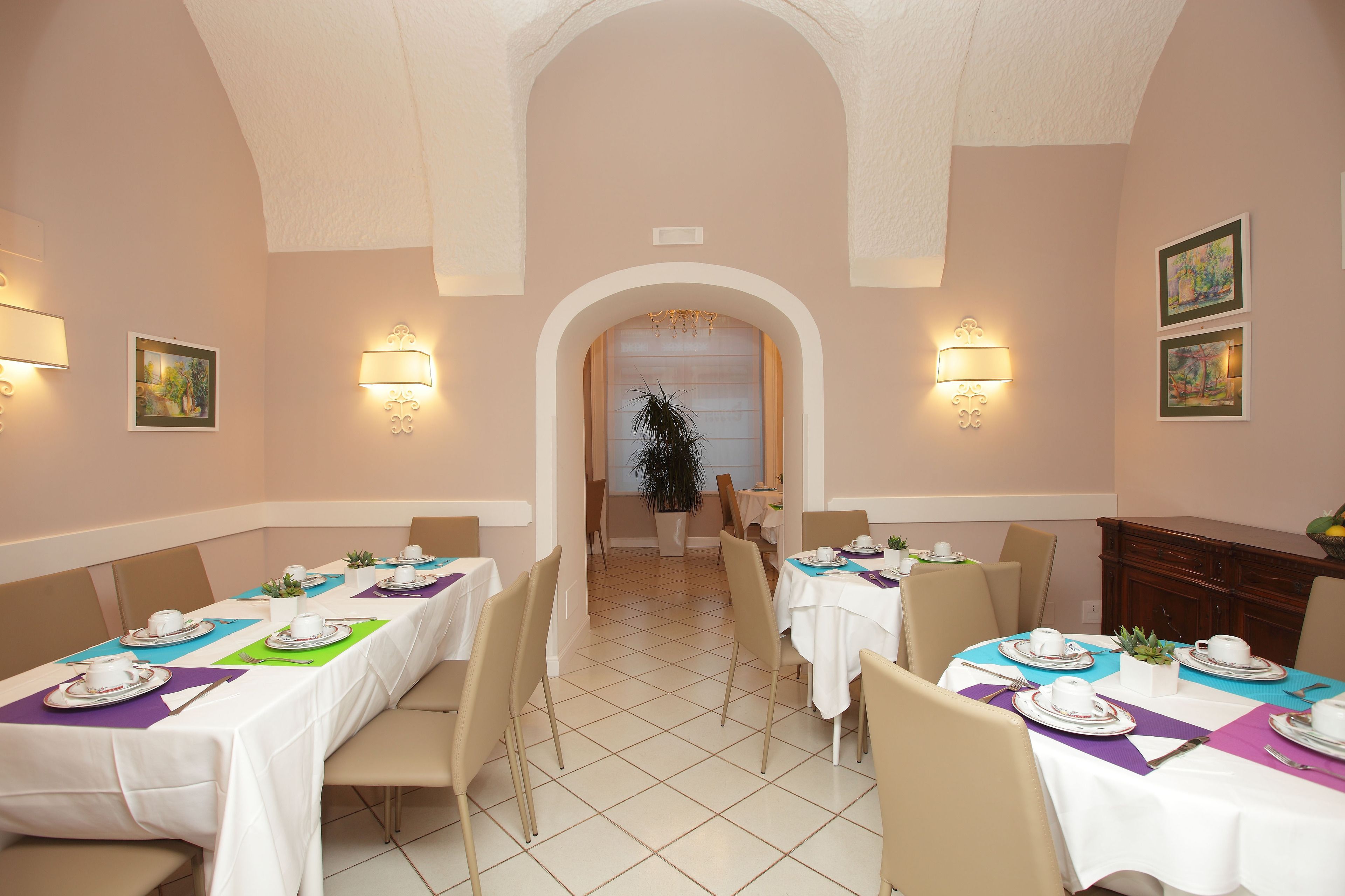 Comedor con mesas dispuestas para una comida, sillas e iluminación instalada en la pared.