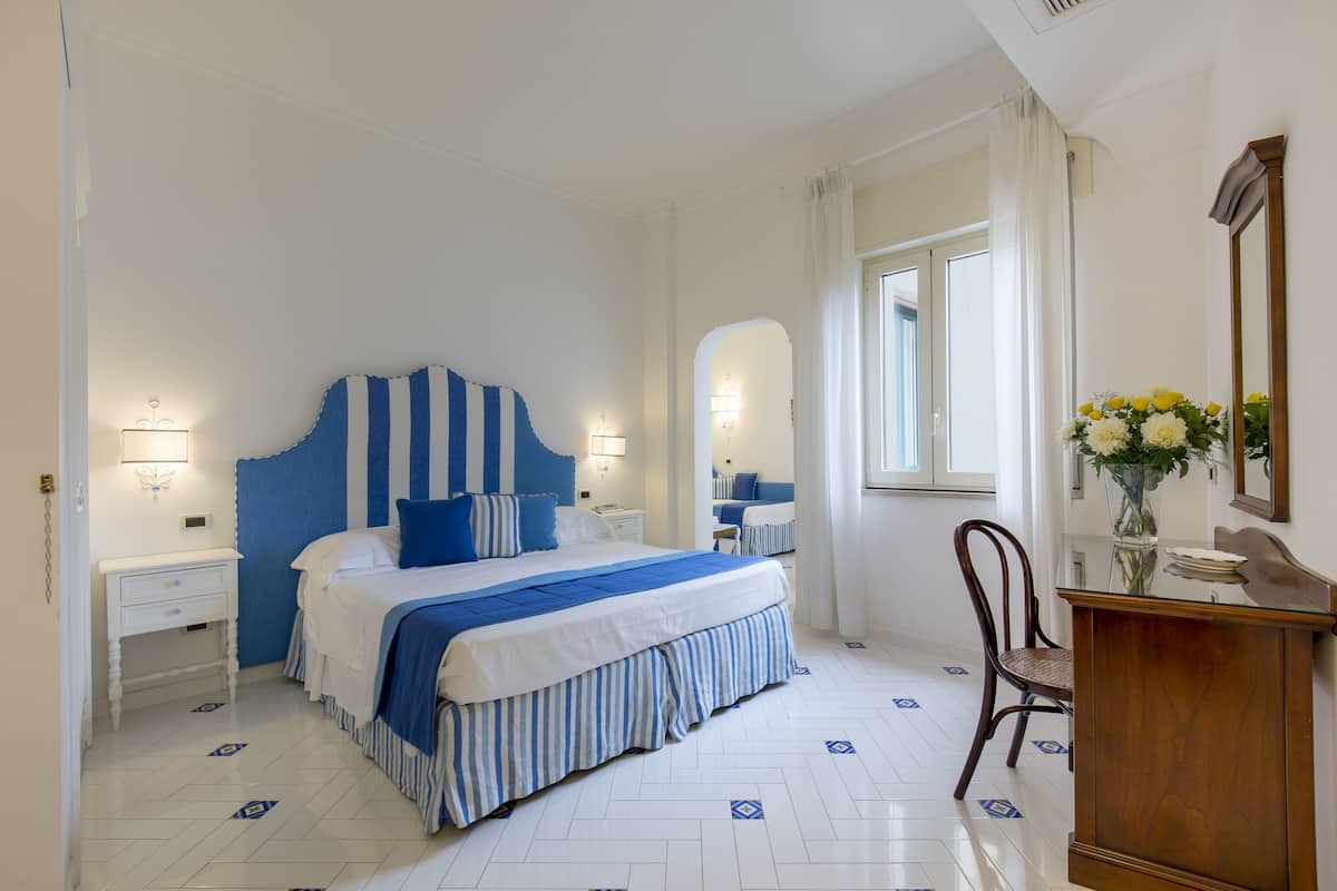 Un dormitorio con cama, mesitas de noche, una silla, cómoda y ventana.