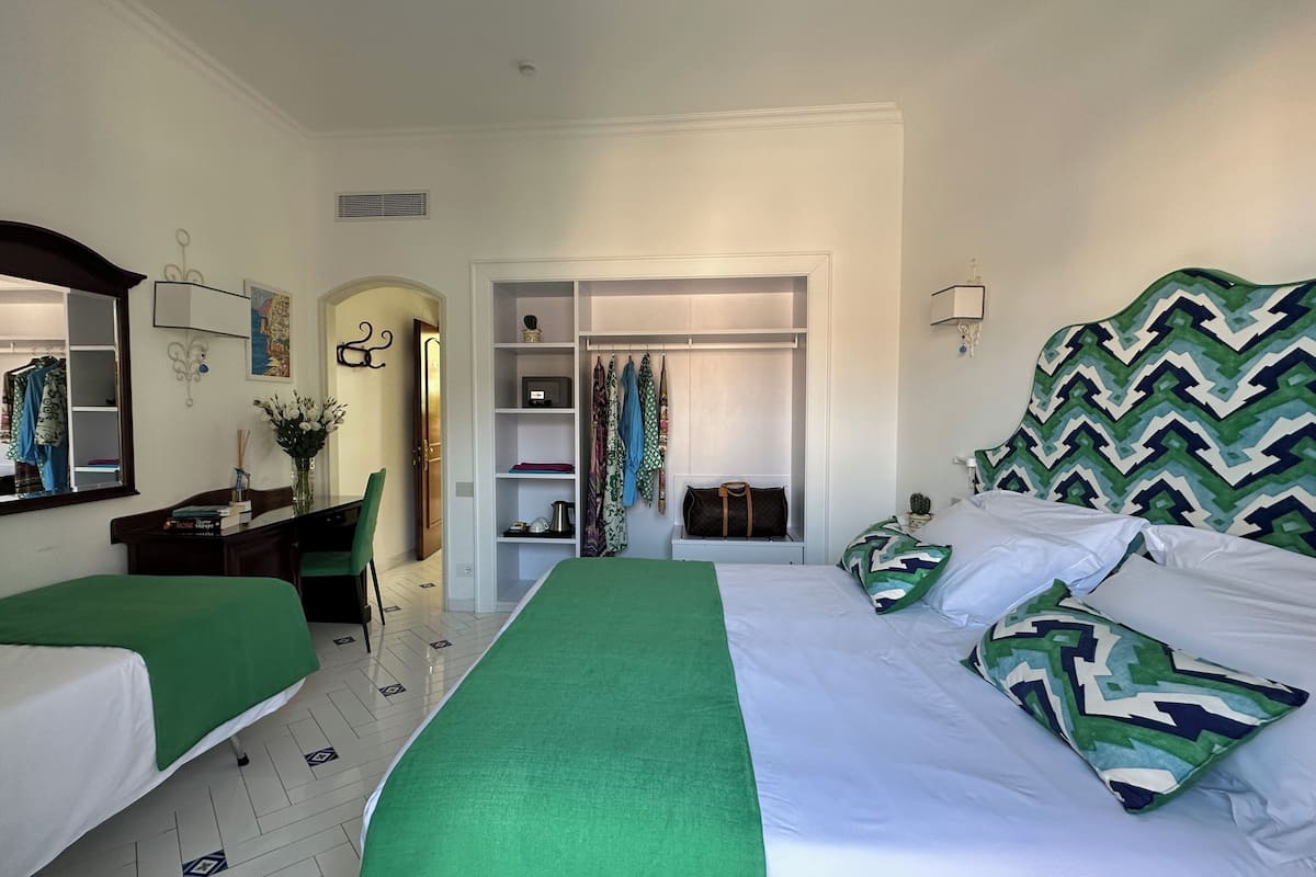 Una habitación de hotel con dos camas individuales, un escritorio con silla, un armario y un espejo.