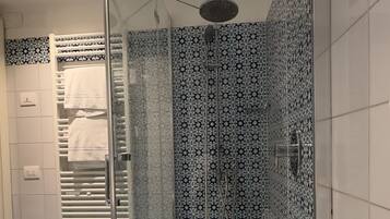 A modern bathroom with a glass-enclosed shower, a white bathtub, and patterned tiles.