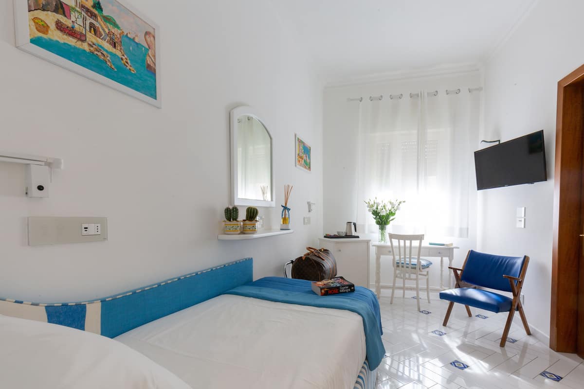 Una habitación de hotel con cama, escritorio, silla, televisor y ventana con cortinas.