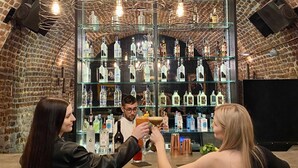 Een bar met een achtergrond van een stenen muur, meerdere hangende lampen en diverse flessen op planken.