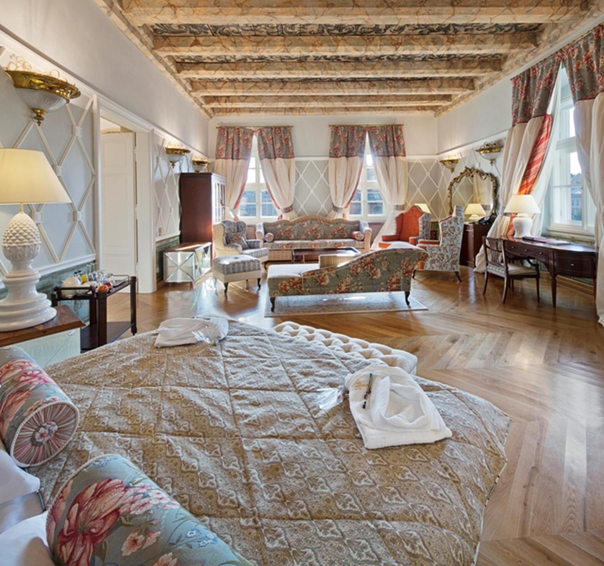 Un dormitorio espacioso con una cama grande, varios rincones de descanso y una araña.