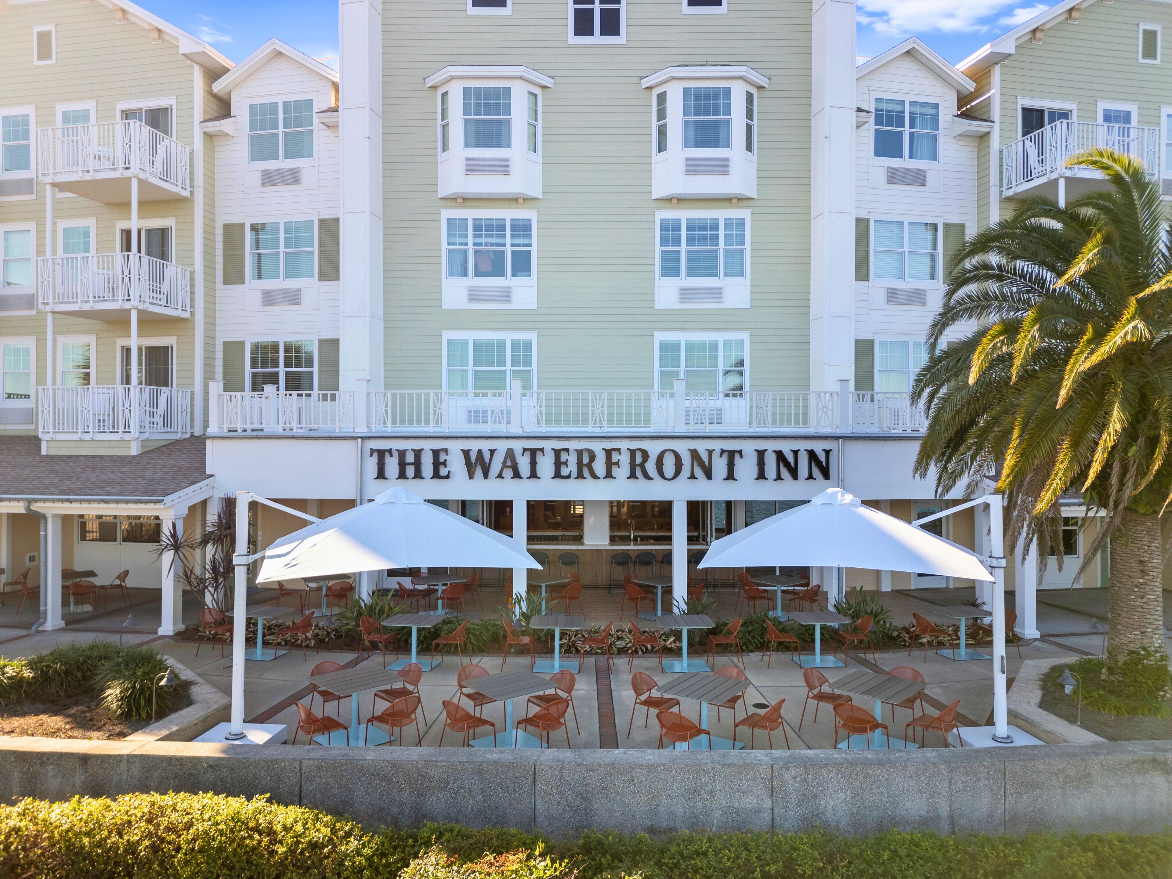 A hotel with a sign reading "The Waterfront Inn" and outdoor seating with umbrellas.