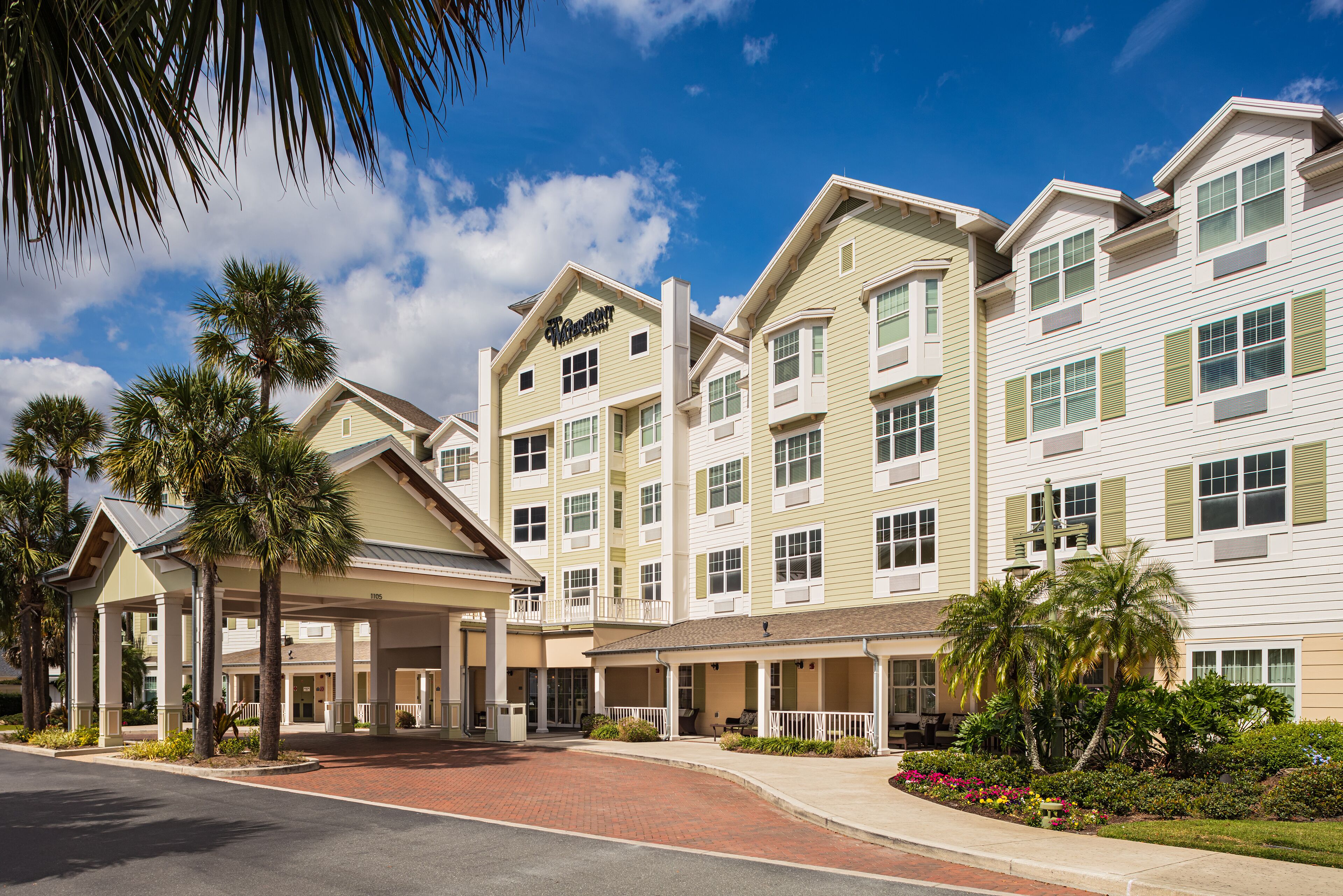 A multi-story hotel with a covered entrance, palm trees, and a brick pathway leading to the entrance.
