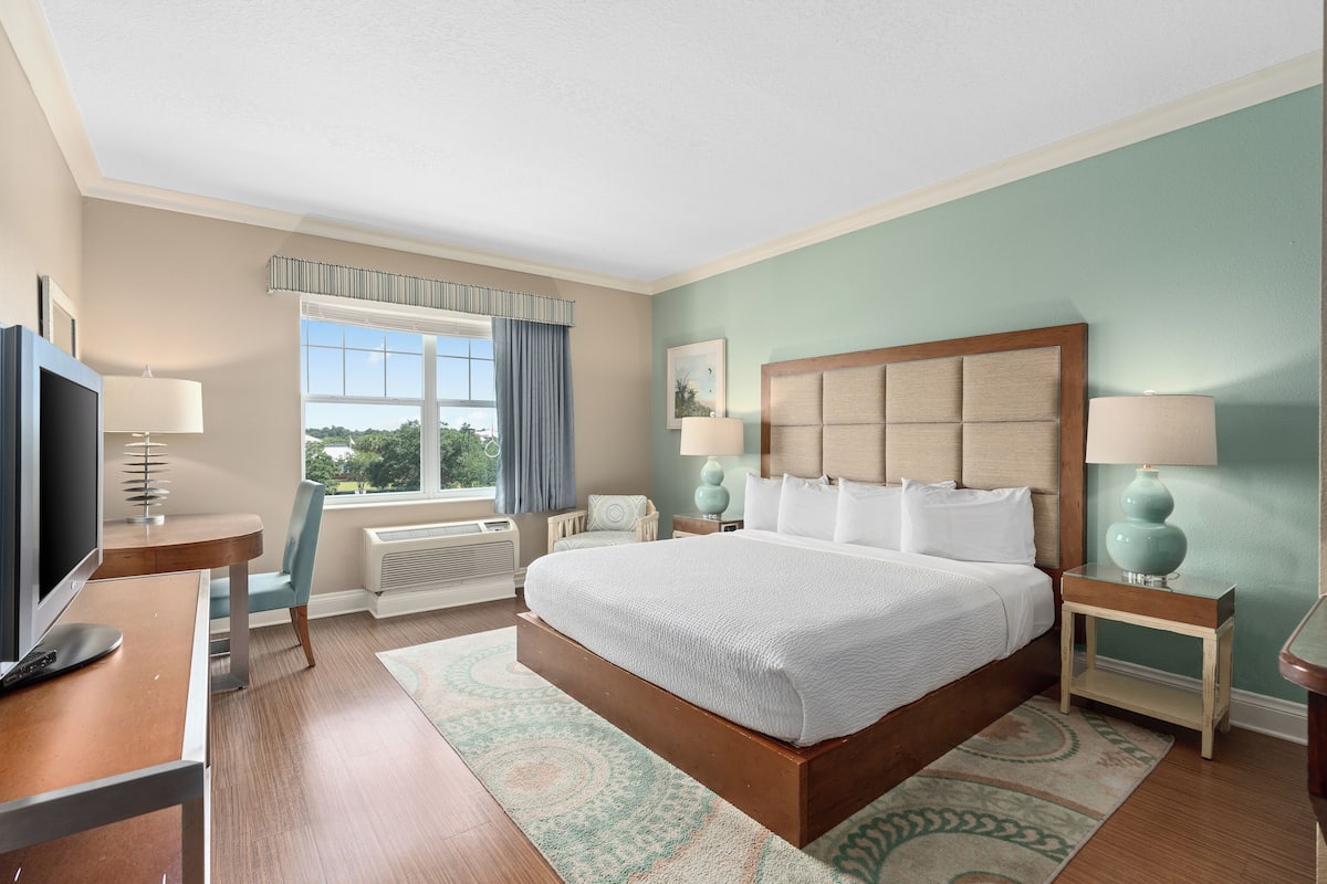 A hotel room with a large bed, a desk with a computer, a TV, and two bedside tables with lamps.