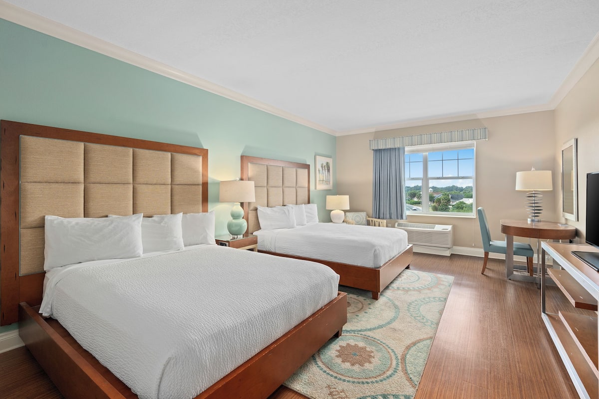 A hotel room with two beds, a desk, a TV, and a window with a view.