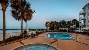 A pool area with two circular pools, surrounded by palm trees and a waterfront view.