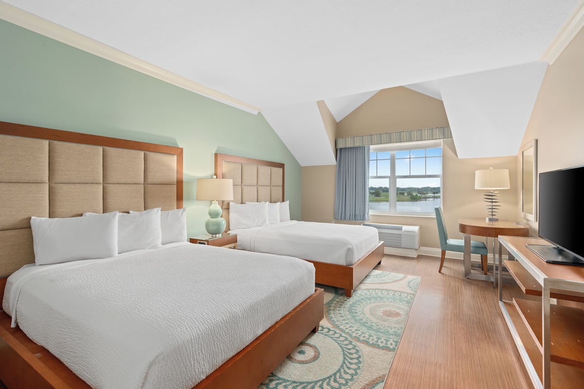 A hotel room with two beds, a desk, a chair, a TV, and a window with a view.