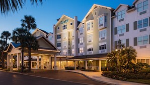 A multi-story hotel with a prominent entrance, a covered outdoor area, and a landscaped garden with palm trees.