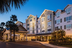 A multi-story hotel with a prominent entrance, a covered outdoor area, and a landscaped garden with palm trees.