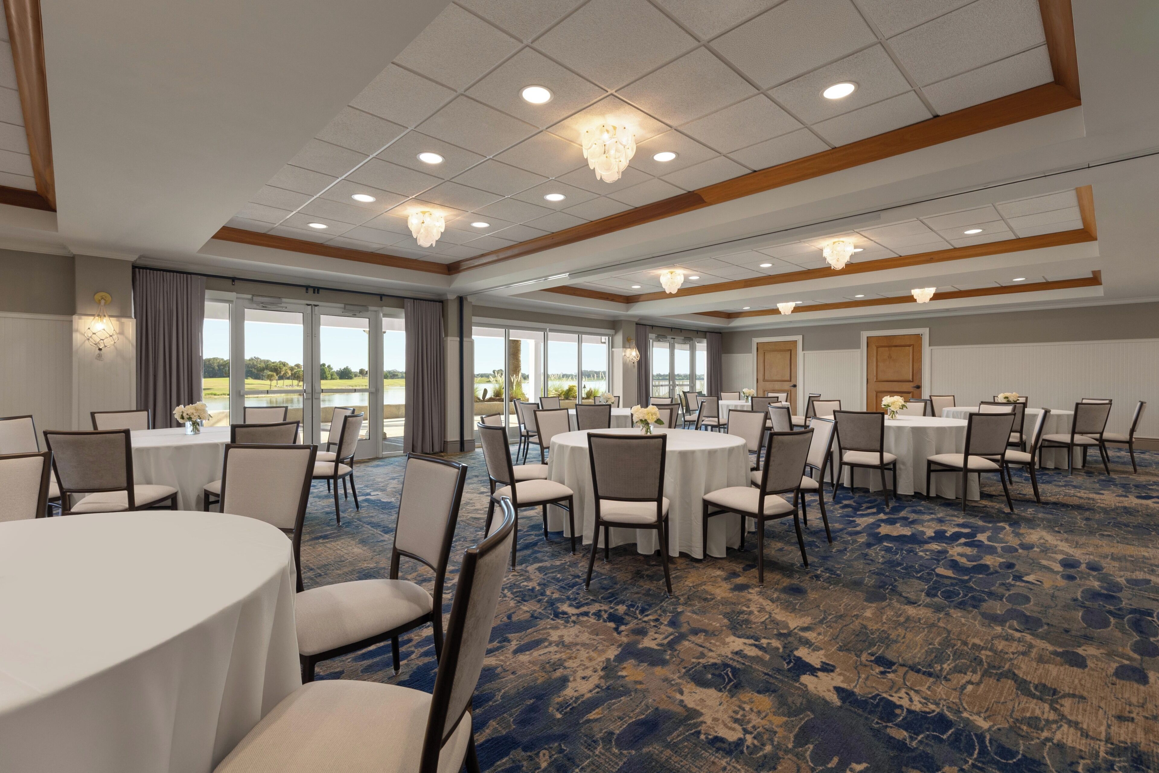 A conference room with round tables and chairs, large windows, and a blue carpet.
