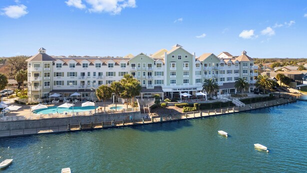 A waterfront hotel with multiple balconies, a pool area, and a view of the water.