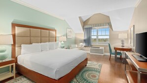 A hotel room with a large bed, a desk with a computer, a TV, and a window with curtains.