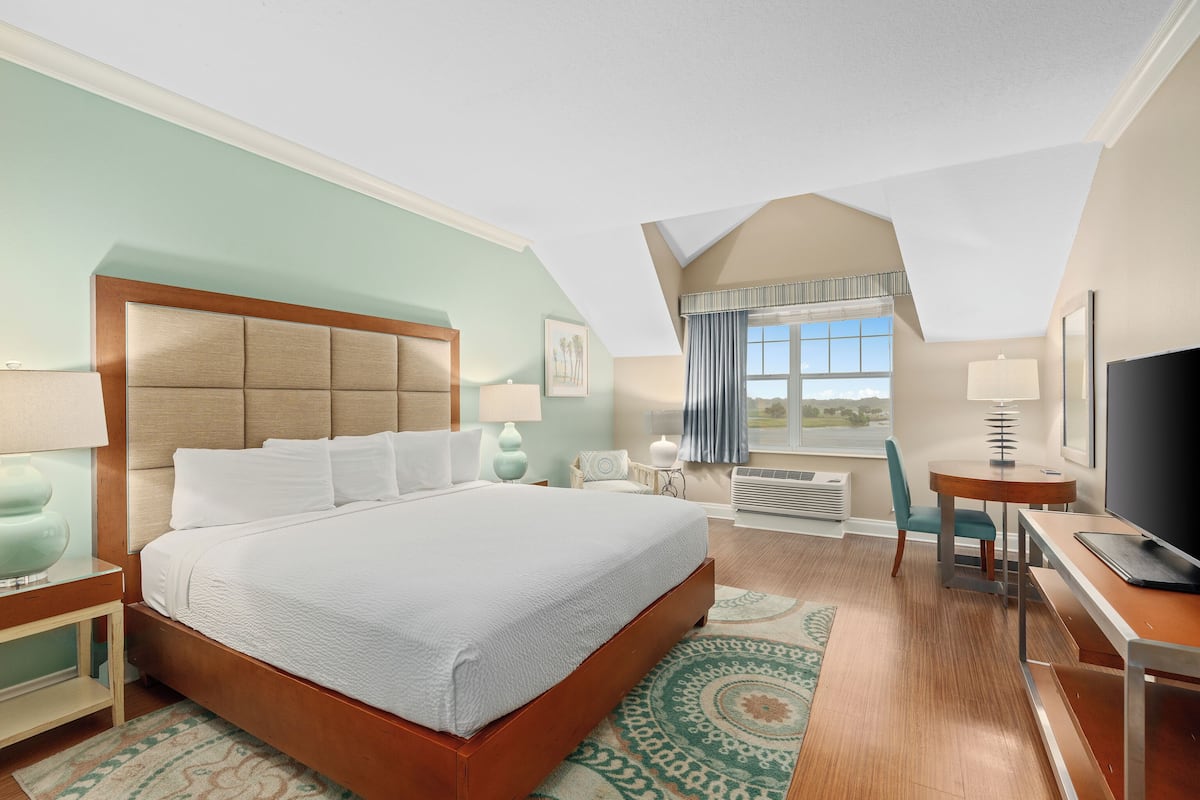 A hotel room with a large bed, a desk with a computer, a TV, and a window with curtains.