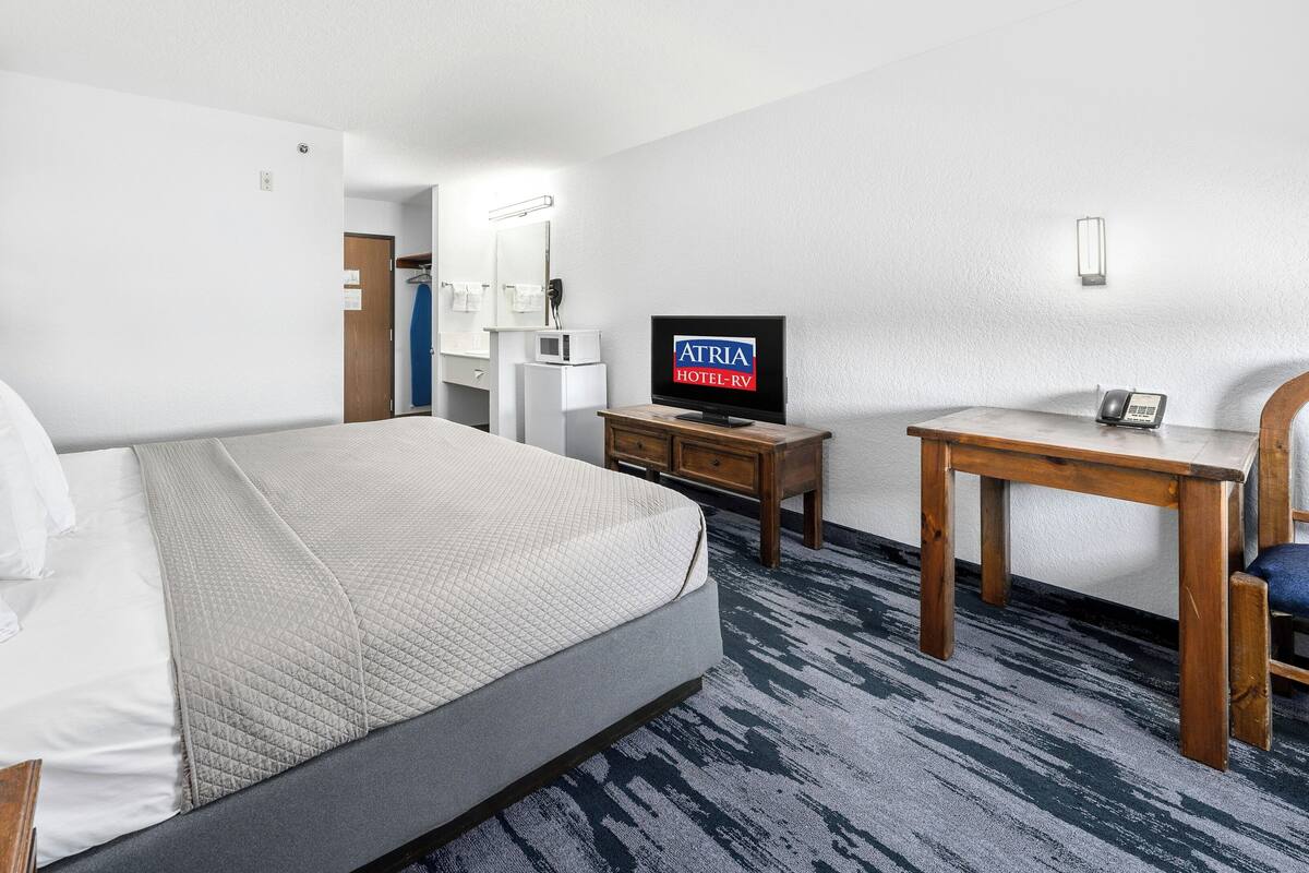 A hotel room with a bed, a desk, a television, and a bathroom in the background.
