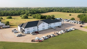 A large building with a parking lot filled with various vehicles, surrounded by green fields and trees. - Atria Hotel and RV McGregor (McGregor)
