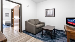 A hotel room with a wooden floor, a gray sofa, a small table, a TV on a wooden stand, and a framed picture on the wall. - Atria Hotel and RV McGregor (McGregor)