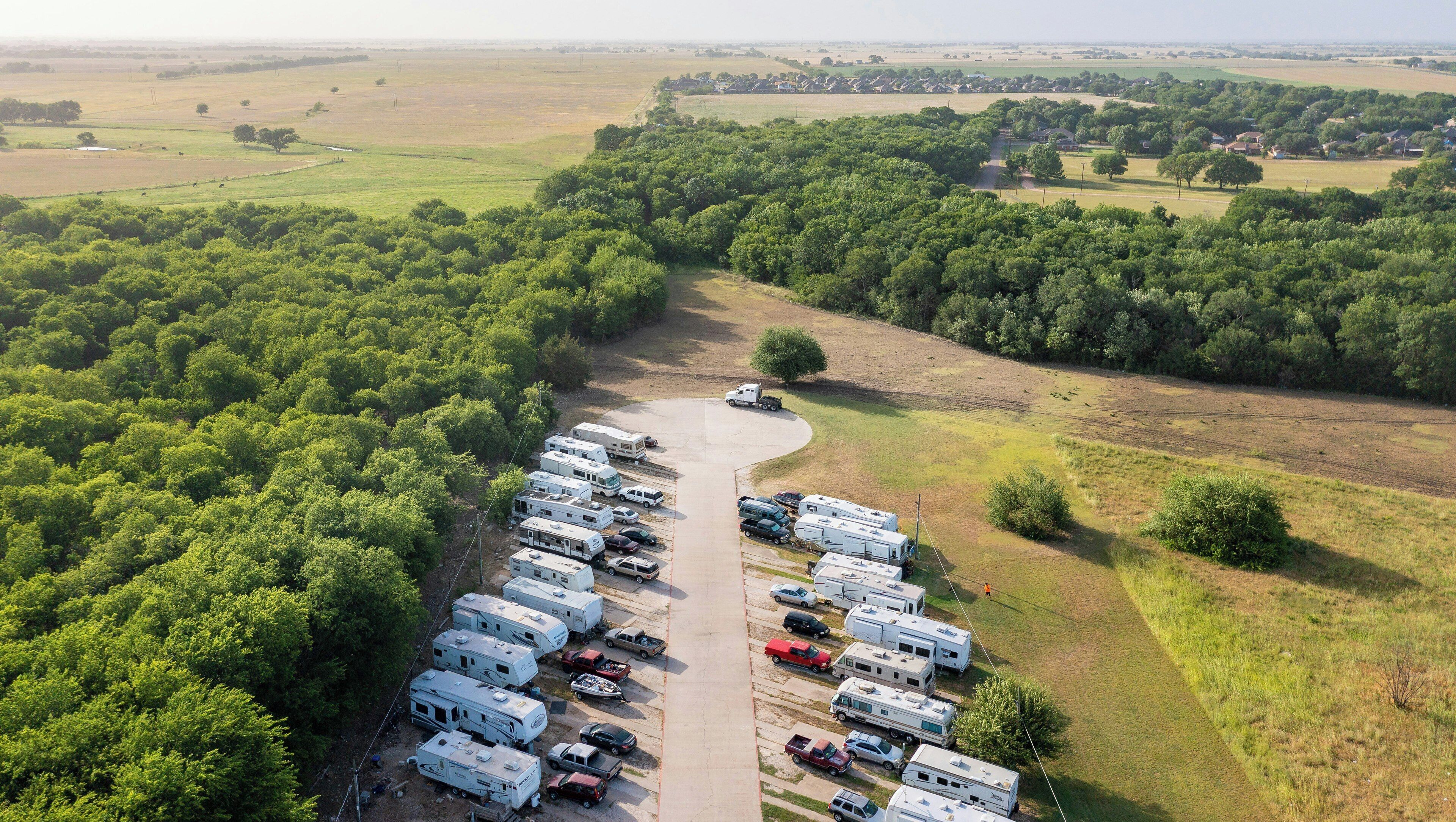 An aerial view of a campground with RVs parked in rows, surrounded by dense forest.