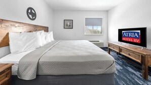 A hotel room with a bed, a TV, a wooden headboard, a picture on the wall, and a window. - Atria Hotel and RV McGregor (McGregor)