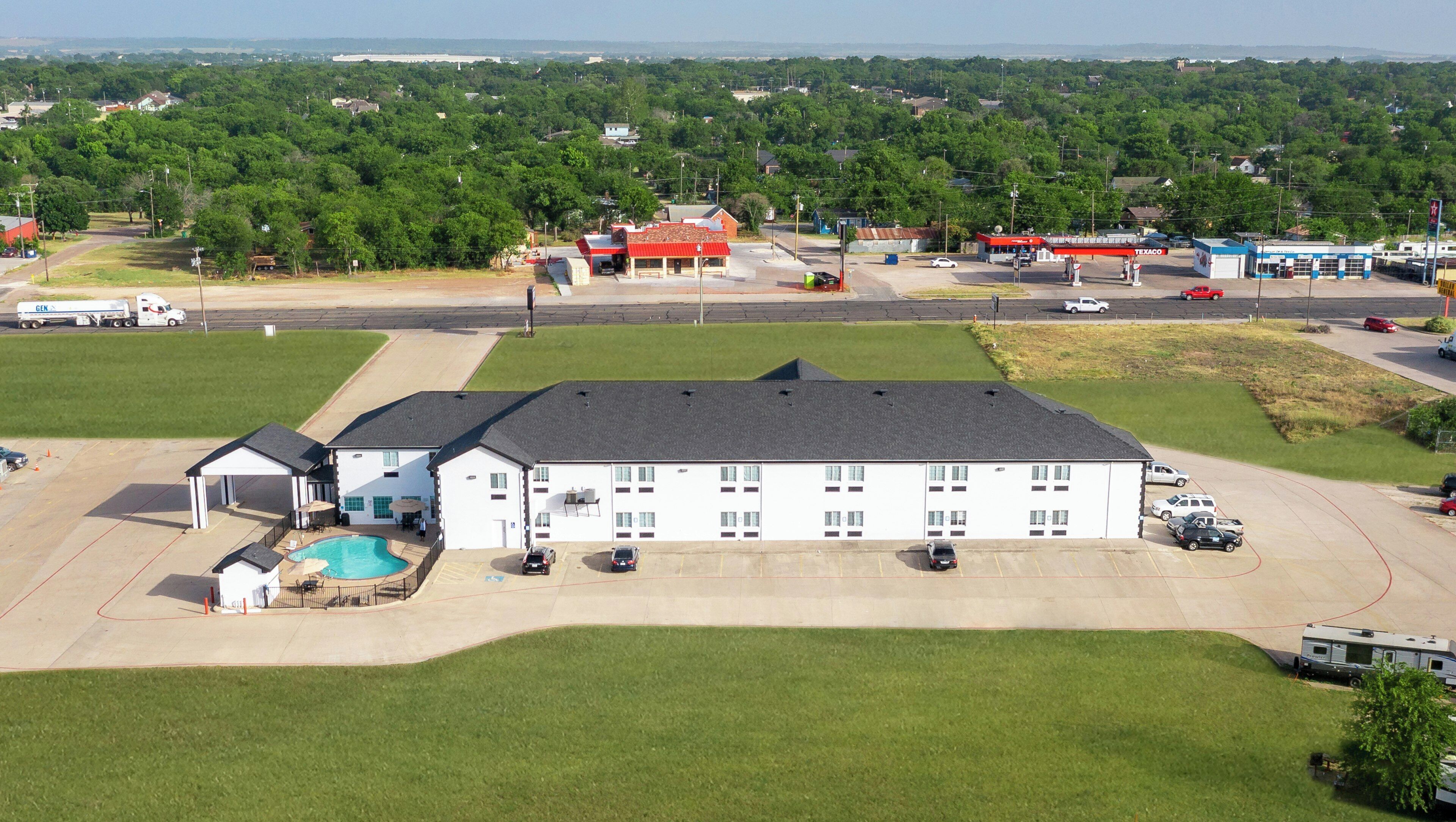 A large building with a swimming pool, a parking lot, and a Texaco gas station in the background.