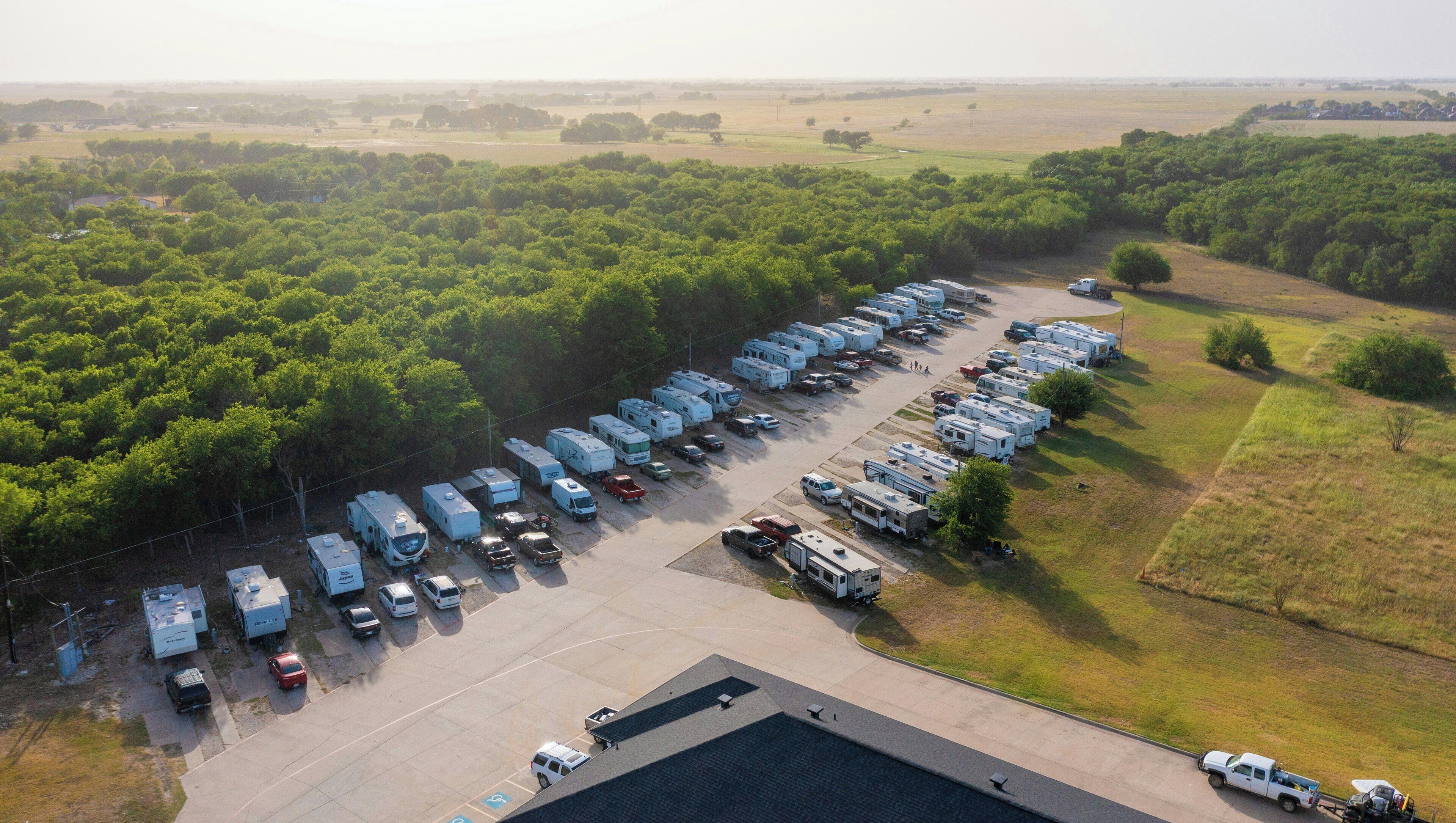 An RV park with multiple RVs parked in rows, surrounded by trees and open fields.