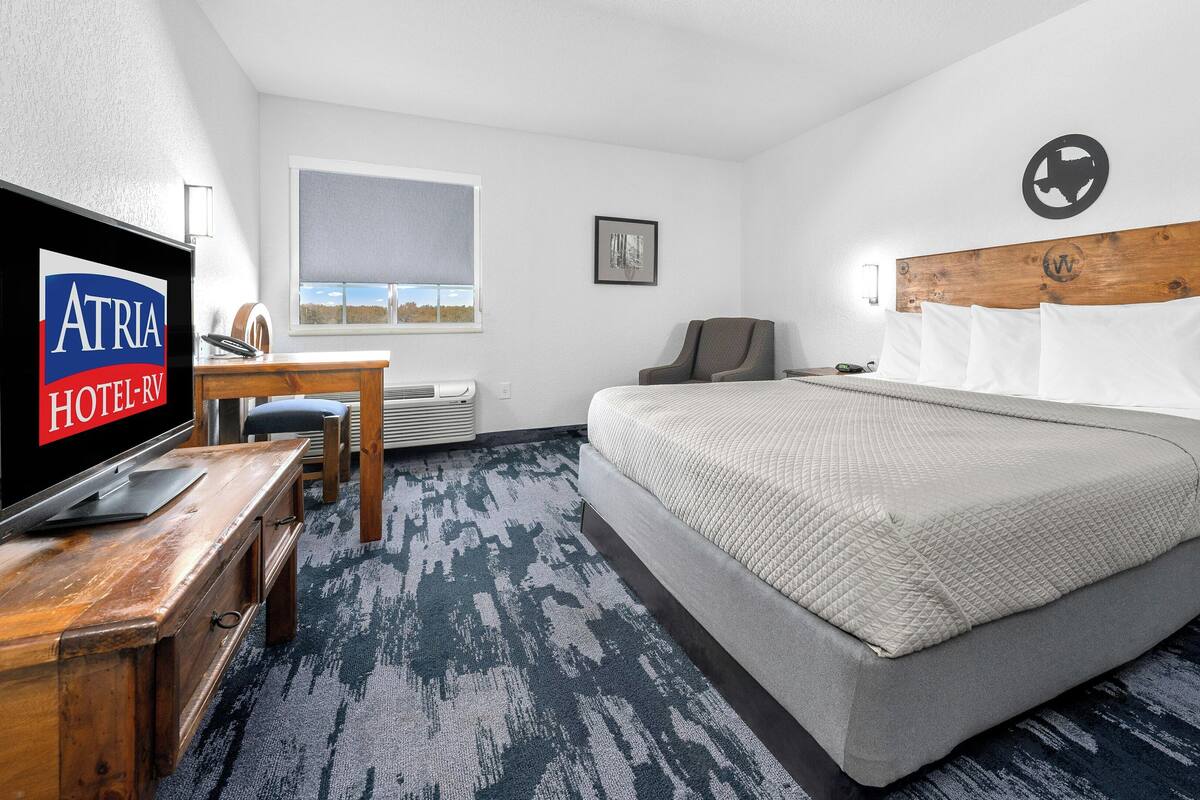 A hotel room with a bed, a desk, a chair, a TV, and a window with a view.
