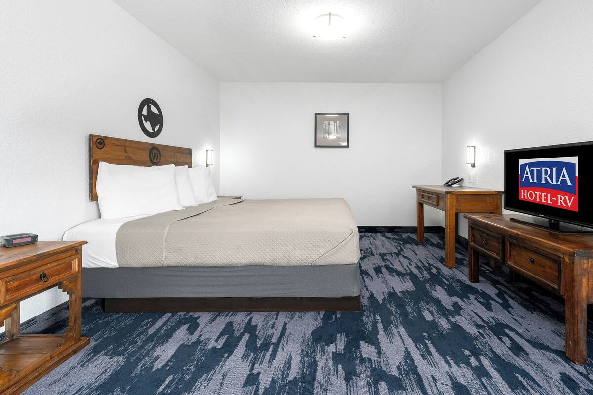 A hotel room with a bed, a television, a desk, and a nightstand.