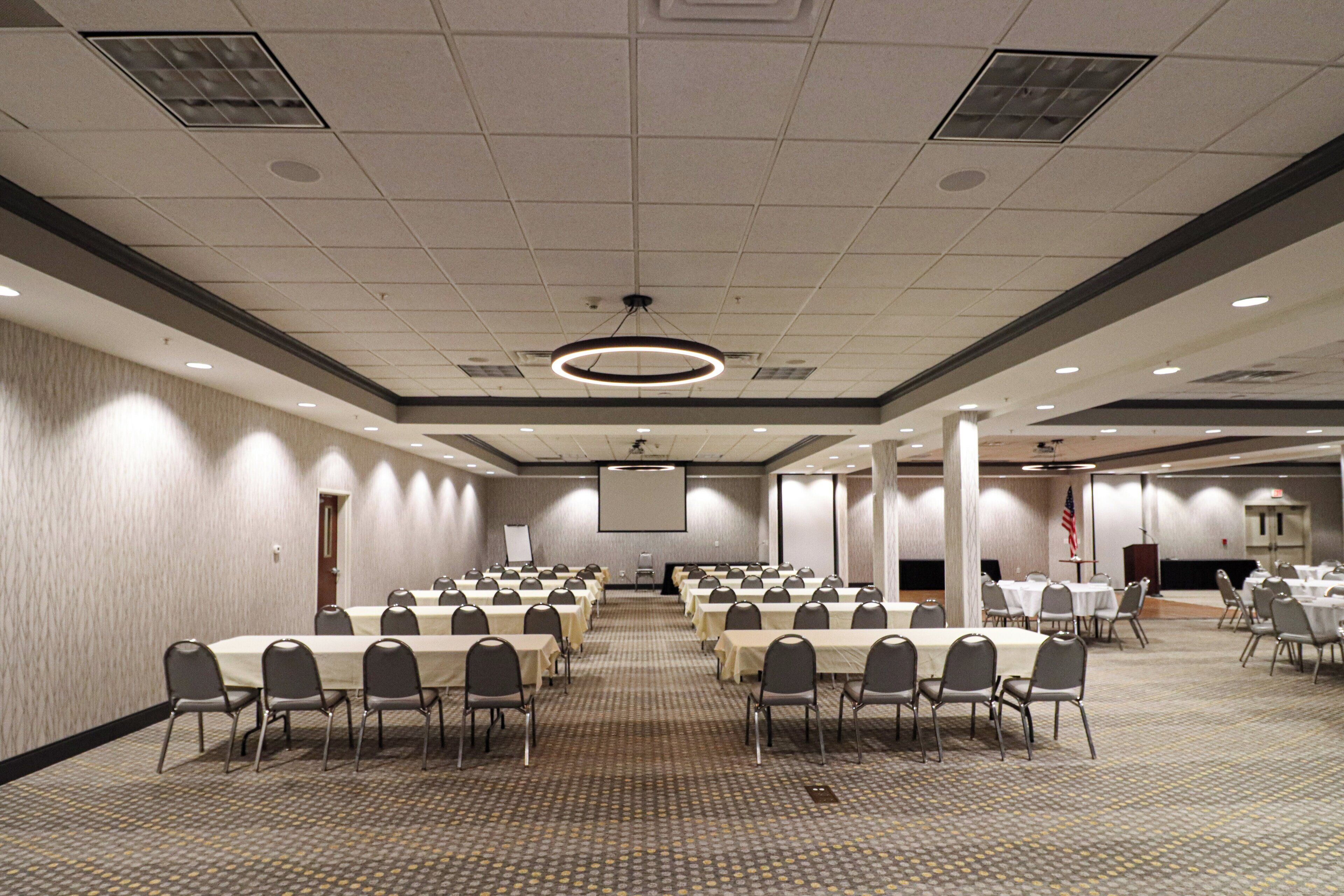 A large conference room with multiple tables and chairs, a projector screen, and a carpeted floor.