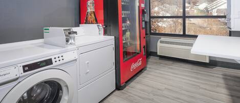 A laundry room with a front-loading washer, a red Coca-Cola refrigerator, and a large window with a view of houses.