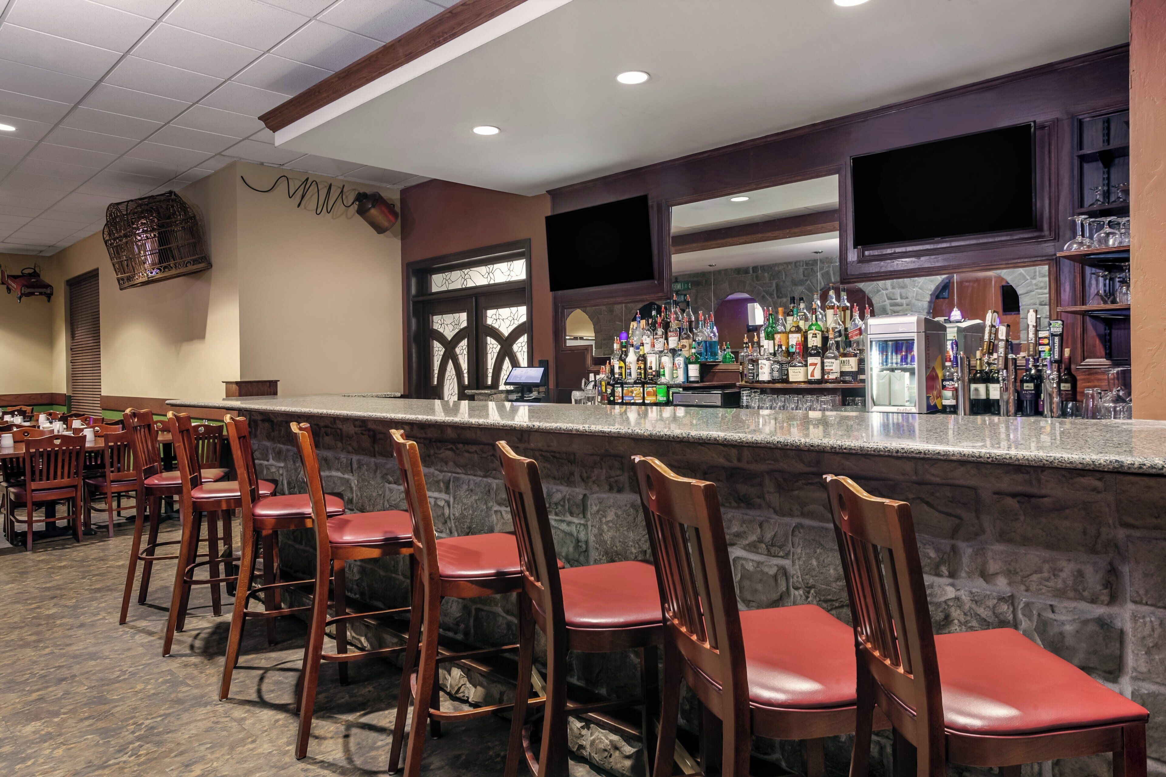 A bar area with a stone counter, wooden chairs, and a variety of bottles.