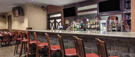A bar area with a stone counter, wooden chairs, and a variety of bottles.