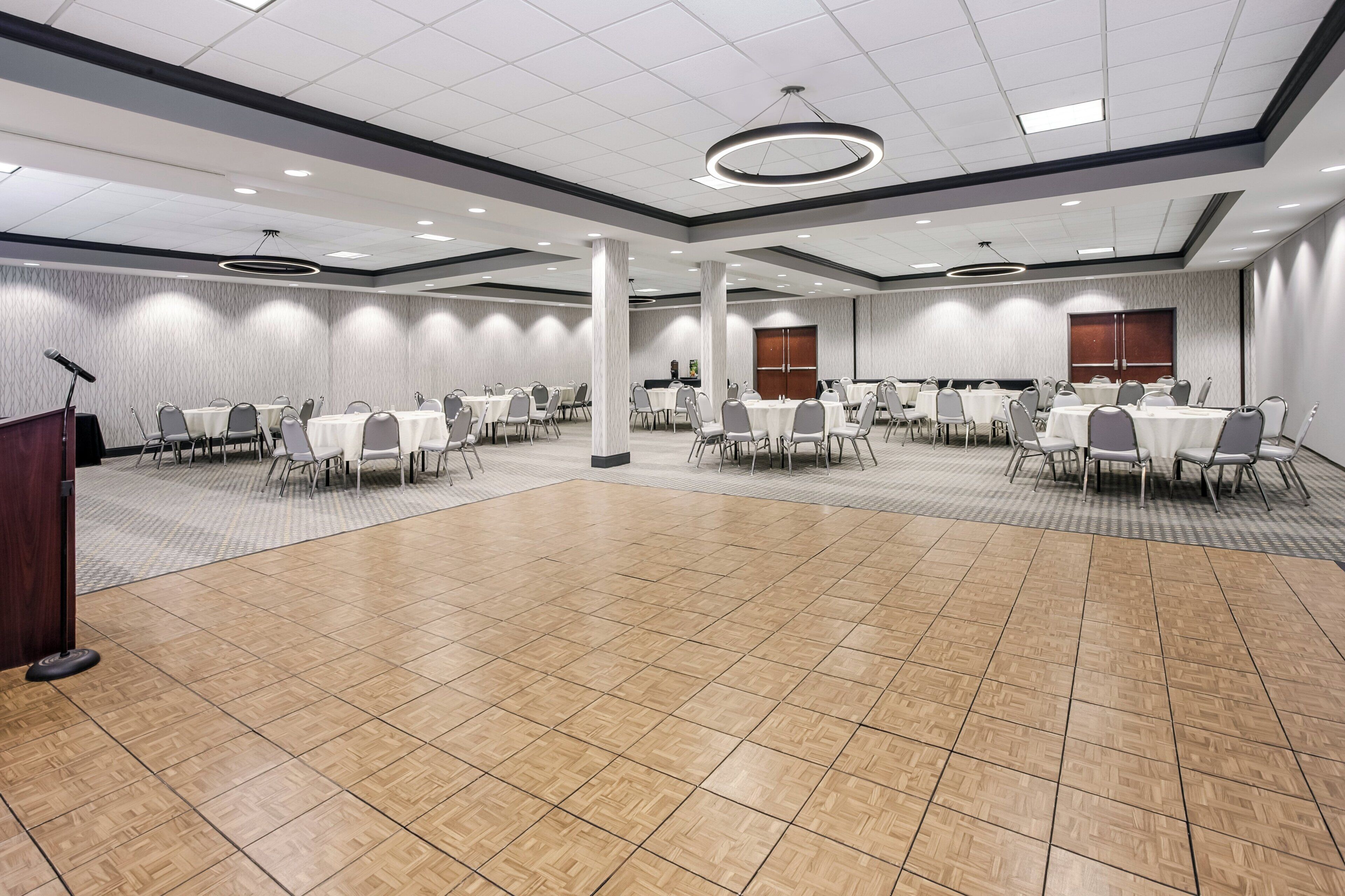 A large conference room with multiple tables and chairs, a podium, and a carpeted floor.