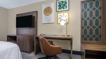 A hotel room with a bed, a desk with a chair, a television, and artwork on the wall.