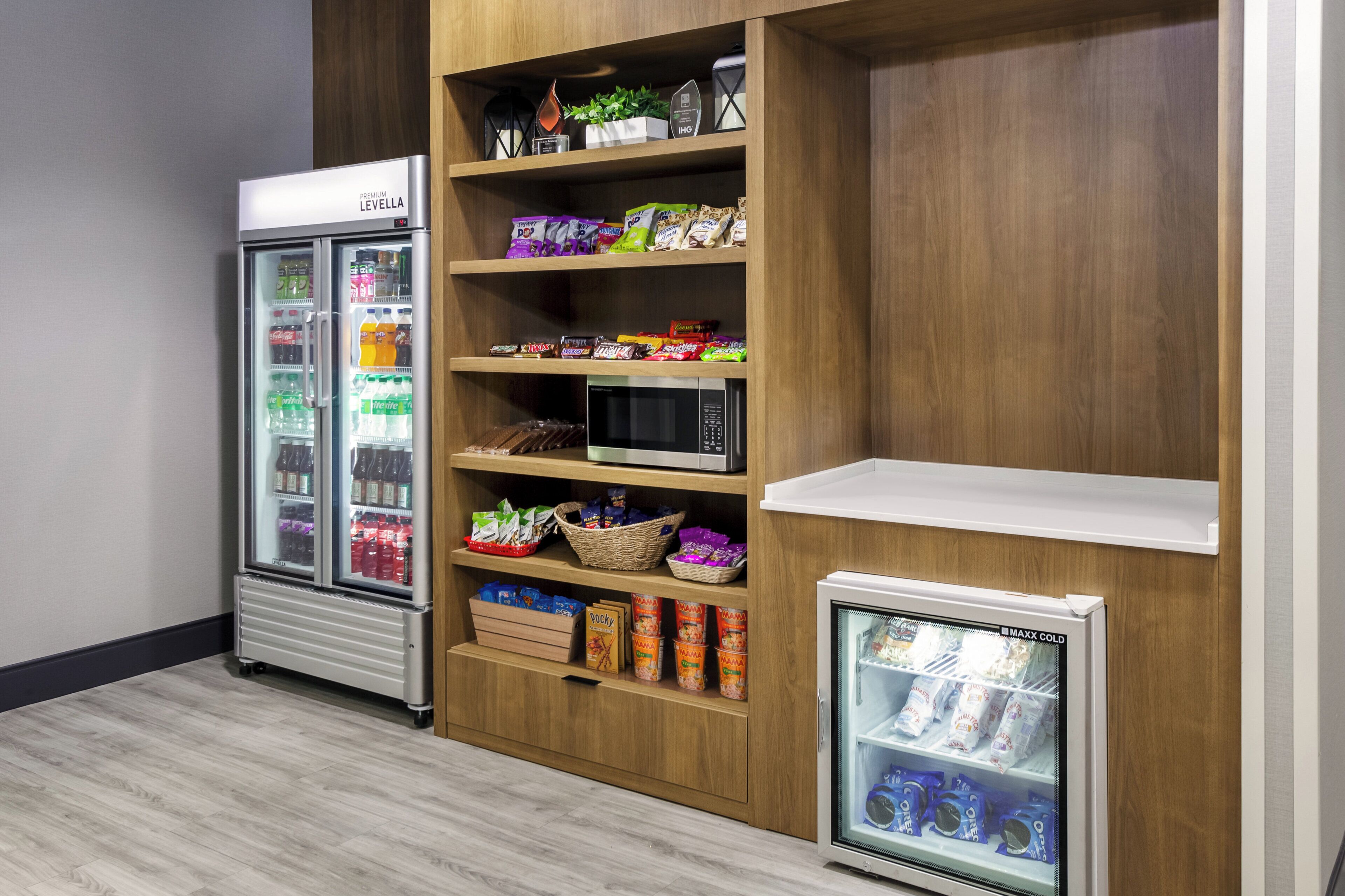 Uma área de vending com dois refrigeradores, um micro-ondas e prateleiras repletas de lanches e bebidas.