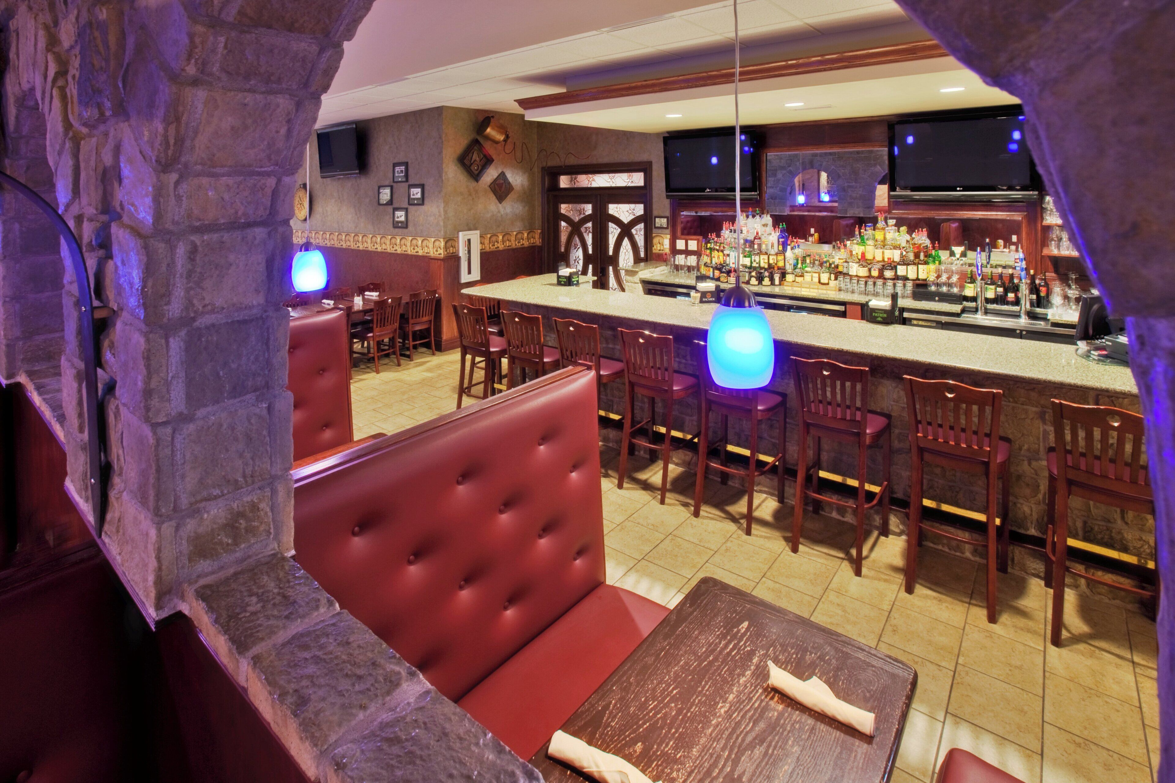 A bar area with a stone wall, wooden bar counter, and seating with red upholstered booths.