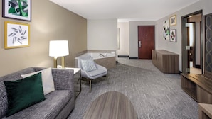 A hotel room with a sofa, armchair, lamp, and a large mirror. - Holiday Inn Quincy East by IHG (Quincy)
