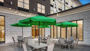 An outdoor patio with tables and chairs, green umbrellas, and string lights. - Holiday Inn Quincy East by IHG (Quincy)