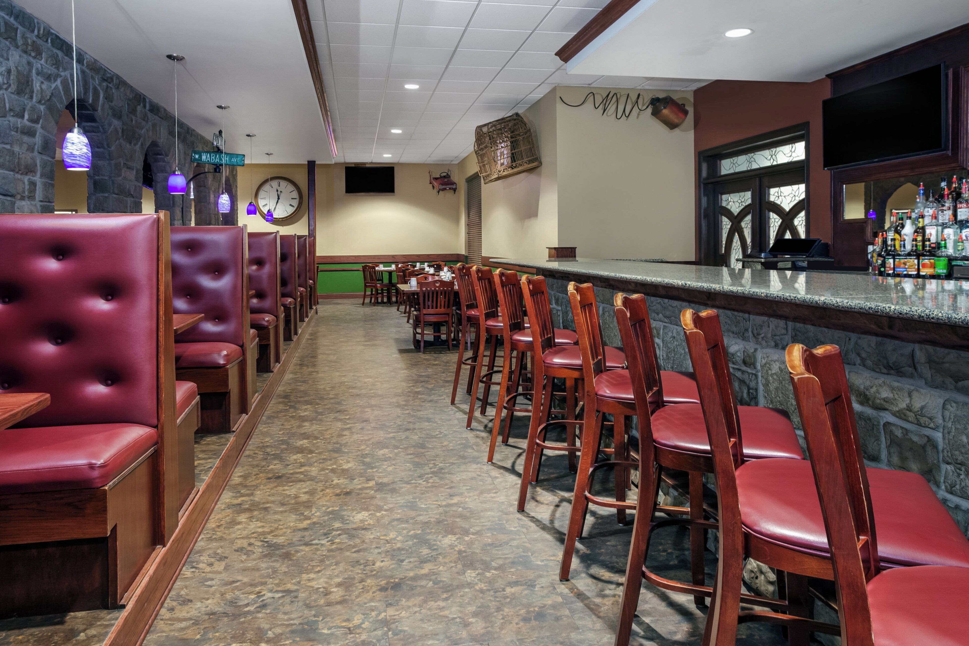 Um restaurante com cabines e mesas altas, um relógio na parede e um bar com diversas garrafas.