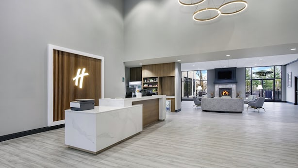 A modern reception area with a marble counter, a wooden panel with a light fixture, a fireplace, and a seating area with a sofa and chairs. - Holiday Inn Quincy East by IHG (Quincy)