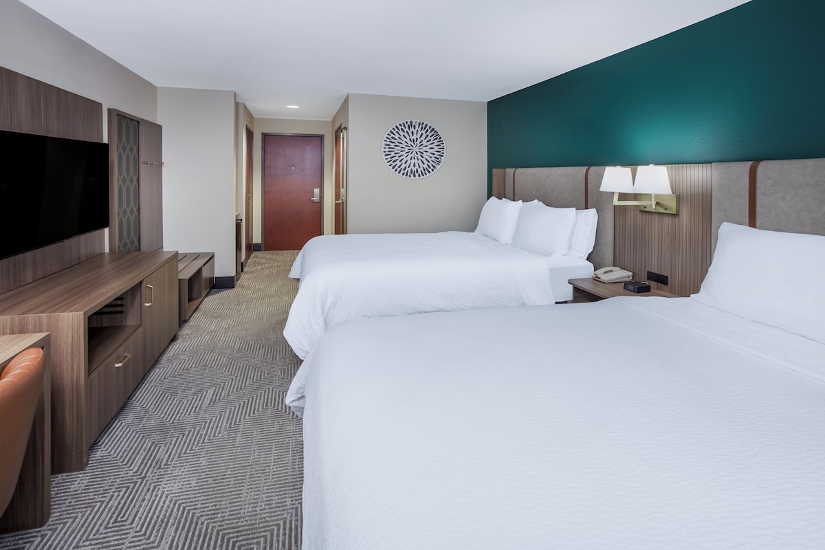 A hotel room with two beds, a desk, a TV, and a decorative wall piece.