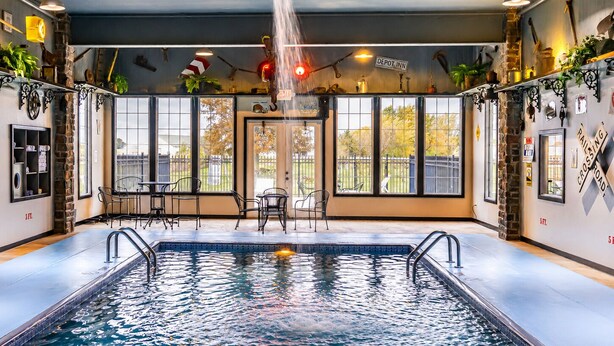 Une piscine intérieure avec vue sur l’extérieur, une enseigne indiquant « Depot Inn », et un panneau « PASSAGE À NIVEAU » sur le mur.
