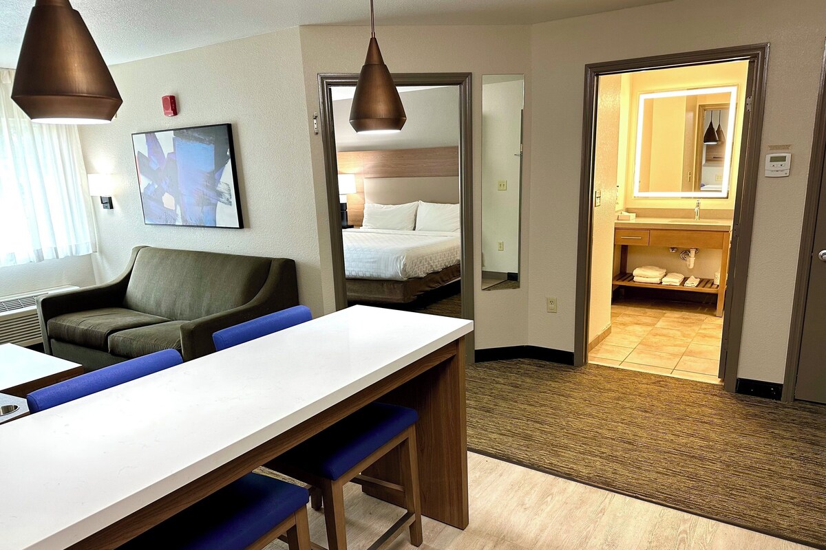 Ein Hotelzimmer mit Essbereich, einem Bett, einem Badezimmer und einem Flur.