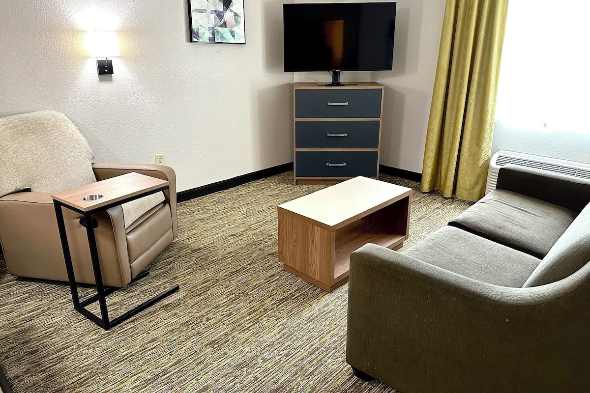 A hotel room with a sofa, a small wooden table, a TV, a cabinet, and a lamp.