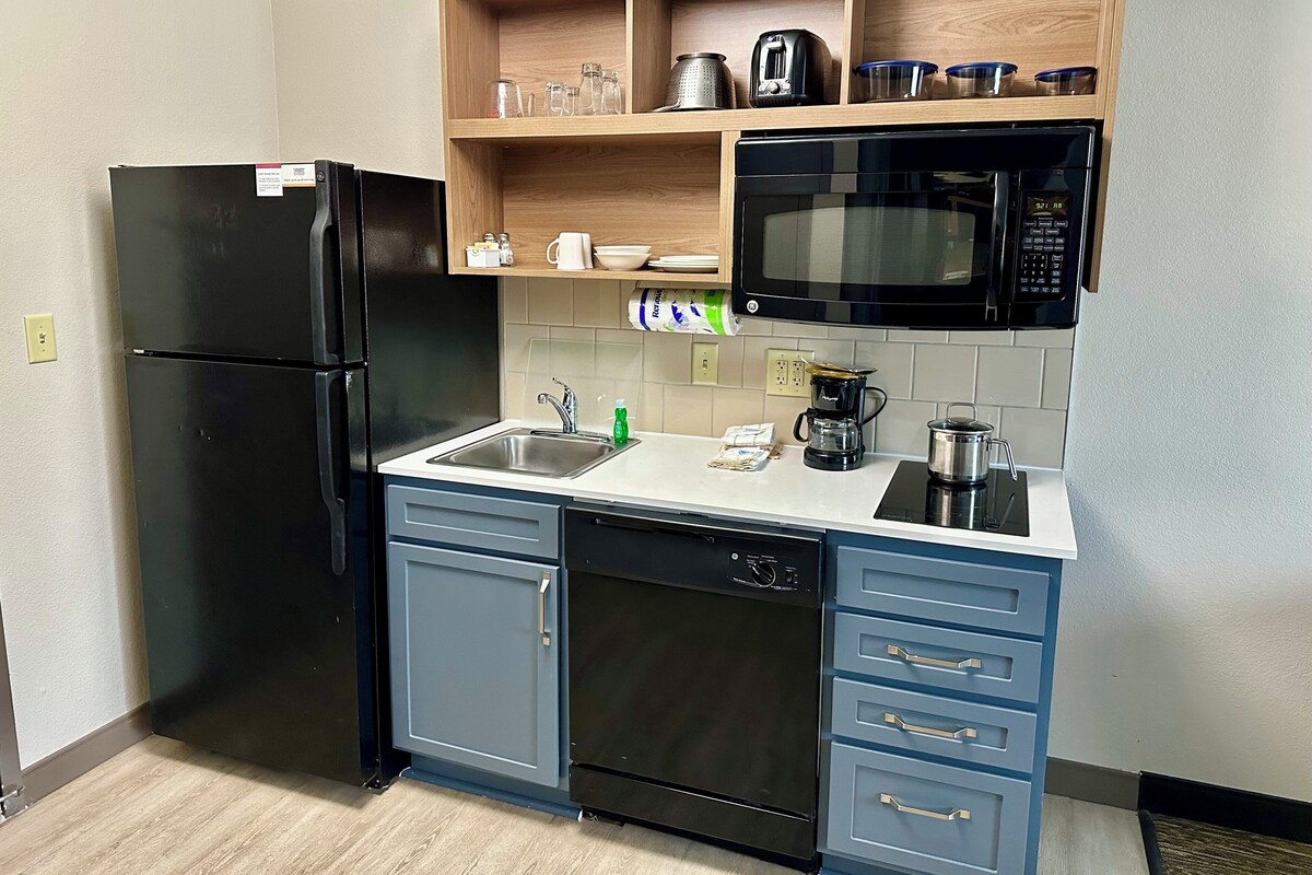 Una cocina compacta con un refrigerador negro, un microondas, una cafetera y un lavavajillas.
