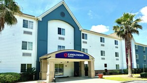 Ett hotell med en blå och vit fasad, en skylt med texten ”Candlewood Suites” och en parkeringsplats med en palmpalm och en blomkruka.
