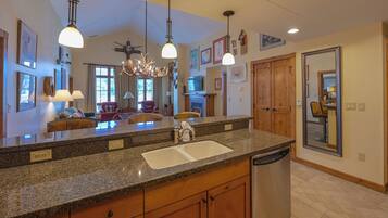 A spacious kitchen with granite countertops, a dishwasher, and wooden cabinets. There are pendant lights, a chandelier, and a large mirror on the wall.