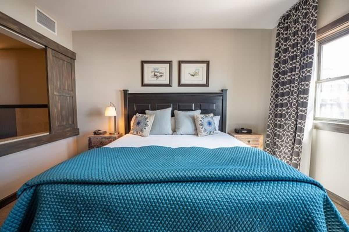 A bedroom with a bed, two framed pictures on the wall, a nightstand, and a window with curtains.
