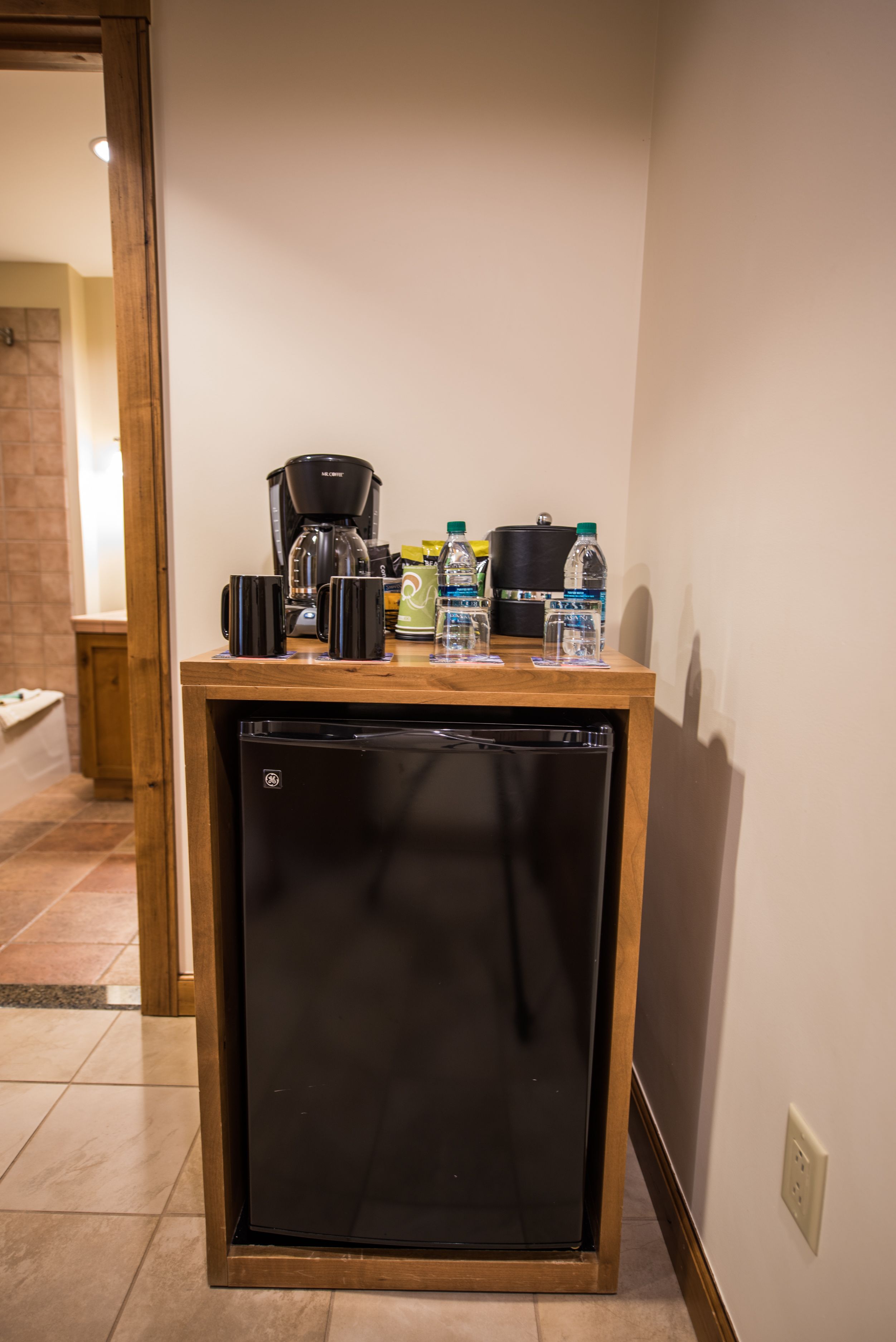 A compact kitchenette with a coffee maker, water bottles, and a small refrigerator.
