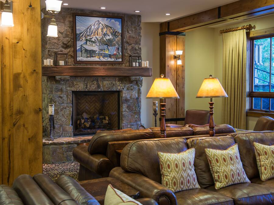 A cozy living room with leather sofas, a stone fireplace, and a mountain painting on the wall.